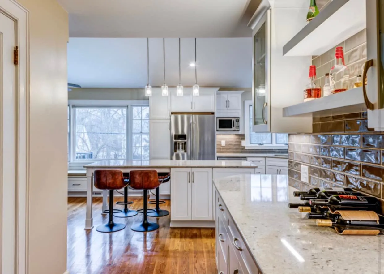 White cabinets with speckled granite counters, glossy taupe subway tile, leather bar stools at the island, and stainless French-door refrigerator.