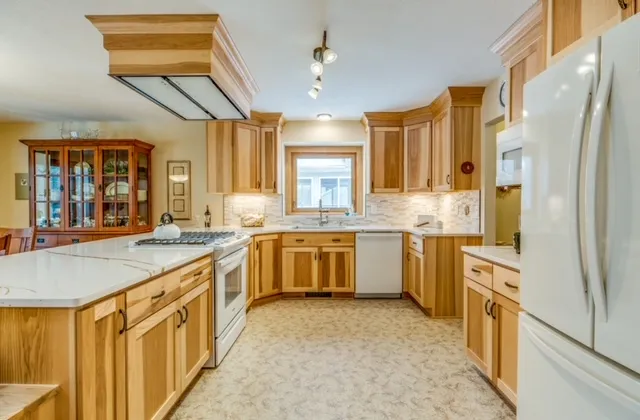 Light hickory cabinets with white quartz counters, mosaic tile backsplash, white appliances, and a glass corner display cabinet.
