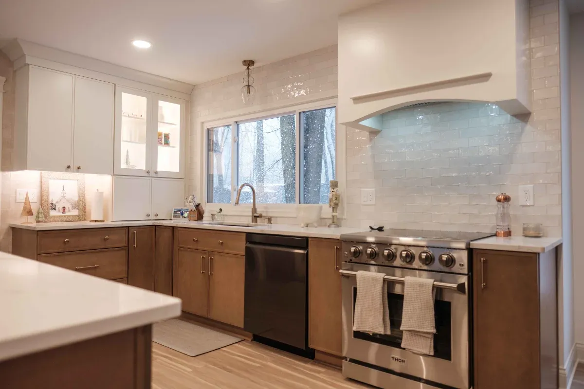 Warm stained cabinets with white counters, glossy white subway tile, a stainless Thor range and hood, and light plank flooring.