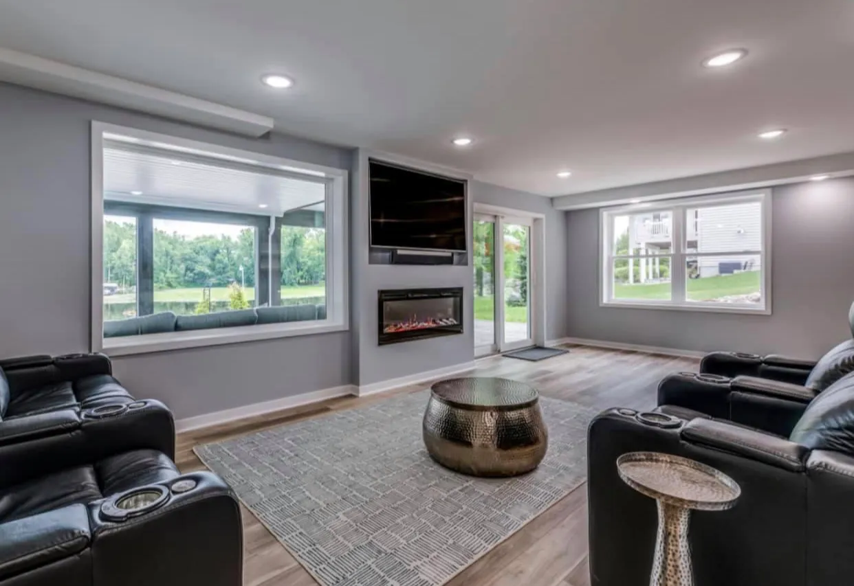 Basement living room with black leather recliners, a linear electric fireplace below a mounted TV, hammered-metal coffee table, and daylight windows.