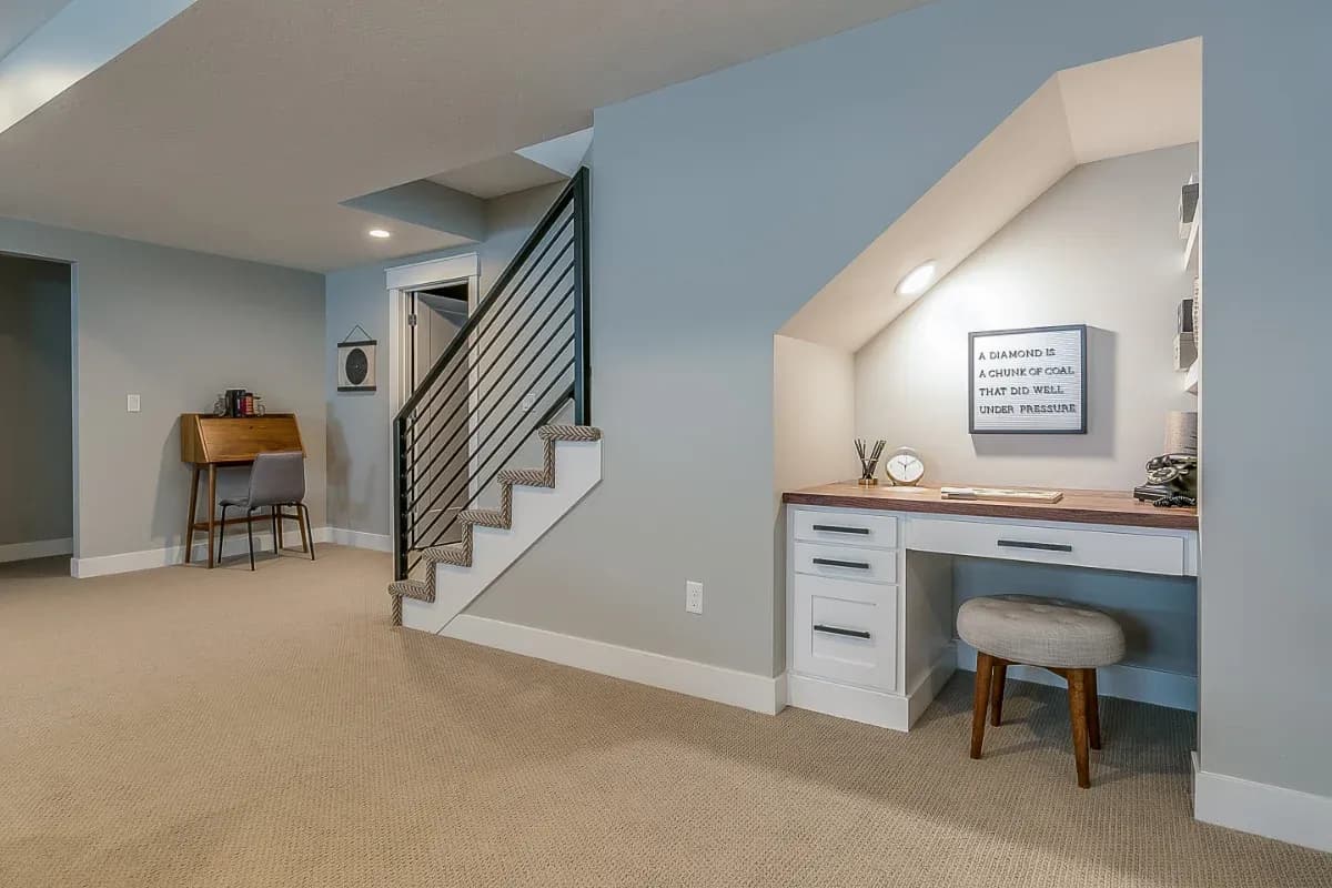 Basement with blue-gray walls, carpet, a horizontal-rail staircase, and a built-in desk nook with a stool tucked under the stairs.