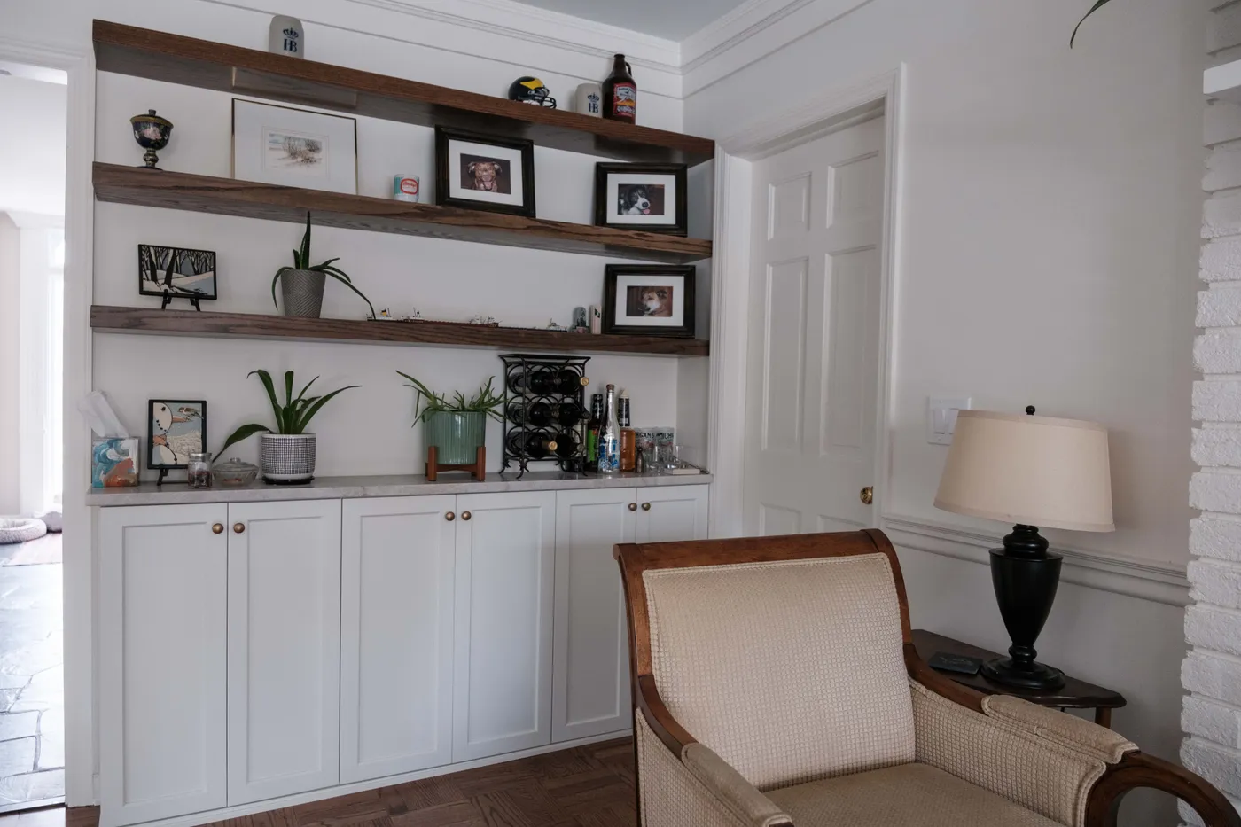Custom white base cabinets with a quartz counter and stained floating wood shelves styled with framed photos, plants, and a wine rack.