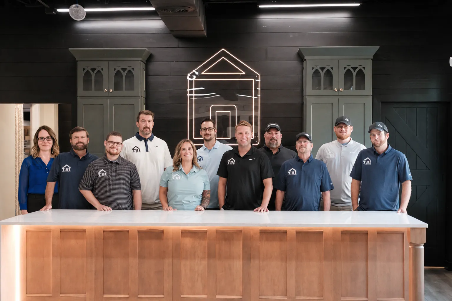 The Teachout Builders team gathered behind the island in their showroom, beneath the lit house-outline sign